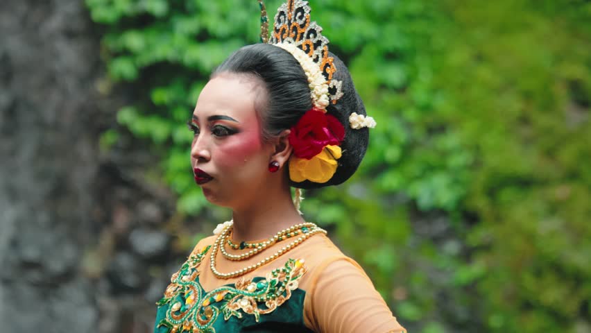 A traditional dancer in a colorful costume, adorned with flowers and intricate jewelry, performing gracefully against a lush green backdrop.
