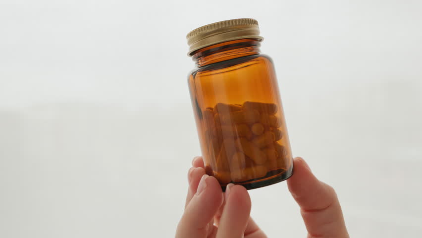 Self-care brown glass bottle filled with pills woman hand holding, healthcare, supplements, wellness. Minimalist background emphasizes focus on health products medication management. Lifestyle