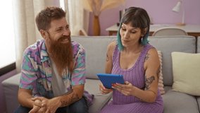 Pregnant woman and man with tattoos sit on couch at home, sharing a moment while using a tablet together in the living room - Powered by Shutterstock - Get 15% off with code: PIKWIZARD15