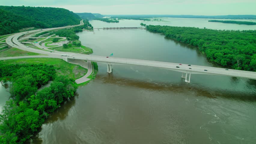 Dry van truck driver on Dresbach Bridge over the Mississippi River, surrounded by lush greenery and waterways. Aerial Wide