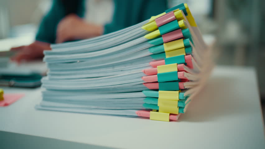 Asian accountant reviews a mountain of paperwork at her desk, feeling the pressure of an impending deadline while managing the demands of her busy work environment