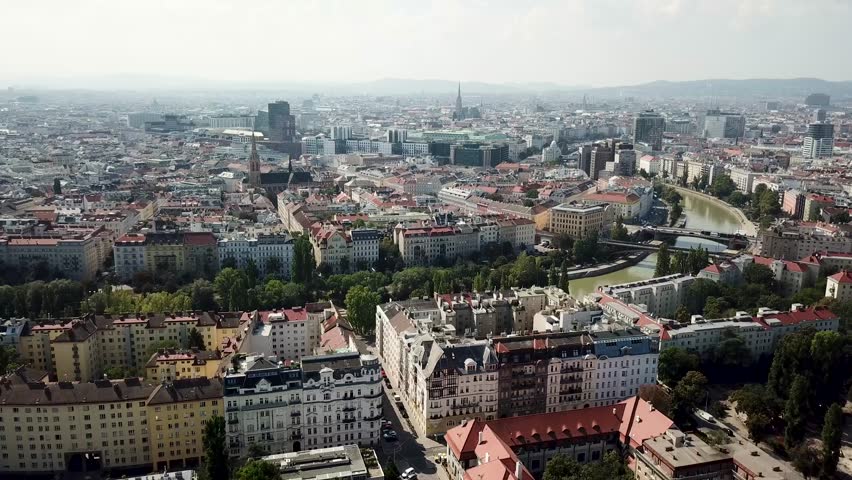 Aerial establishing shot of old apartment houses with river view in Vienna City, Austria. Cityscape with old town and church in summer. Forward wide shot.