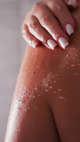 Woman cleans skin with scrub in shower unit closeup. Lady uses natural cosmetic product to exfoliate dry skin in bathroom. Beauty routine at home