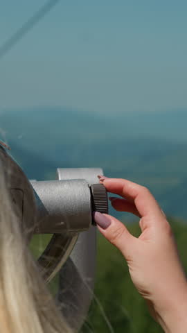 Female tourist adjusts modern tower viewer on point at cable way station against foggy old mountains close backside view slow motion