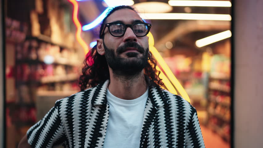 Portrait of Energetic young man gesturing enthusiastically in front of a neon-lit shop, exuding charisma and confidence. His joyful expression and lively backdrop reflect vibrant urban lifestyle