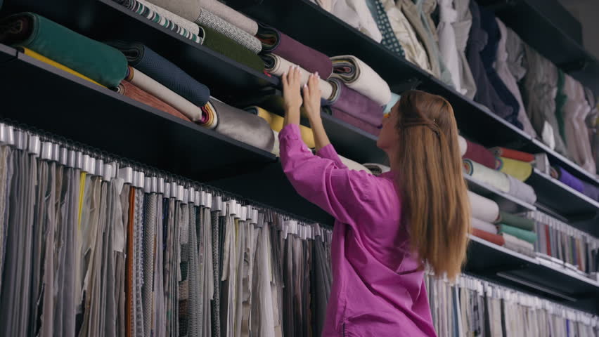 Caucasian woman shopper customer choosing fabrics on shelves in cloth store girl shopping choose soft linen satin silk tissues natural luxury fashion materials for house interior textile shop atelier