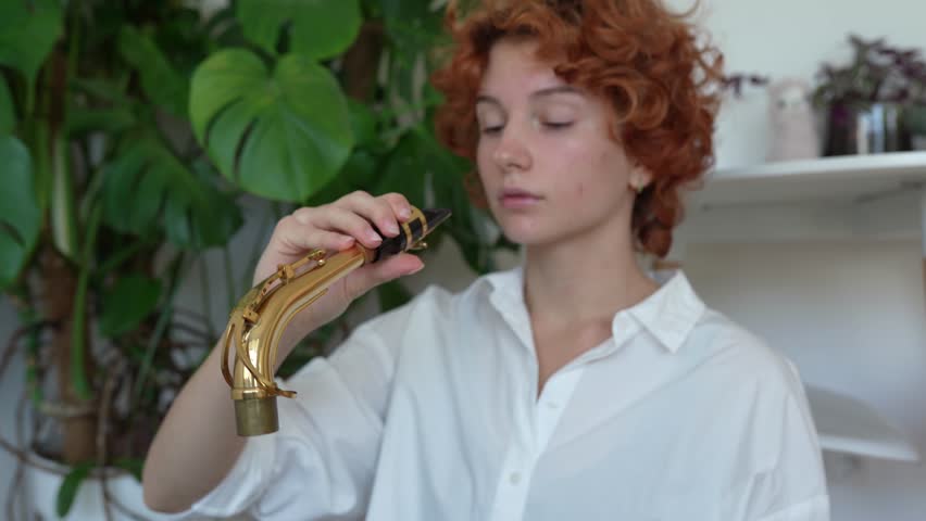 young red-haired woman musician sitting on floor preparing musical instrument saxophone to play. care of a wind musical instrument, music training