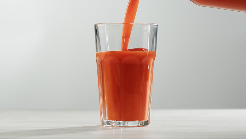 Woman pouring carrot juice from jug into glass at wooden table, closeup