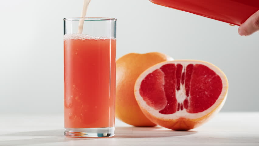 Woman pouring grapefruit juice from juicer into glass on colorful background, citrus vitamic c healthy fresh juice in cafe, morning breakfast drink.