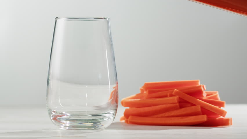 Woman pouring carrot juice from jug into glass at wooden table, closeup