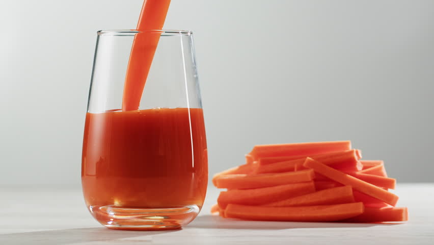 Woman pouring carrot juice from jug into glass at wooden table, closeup