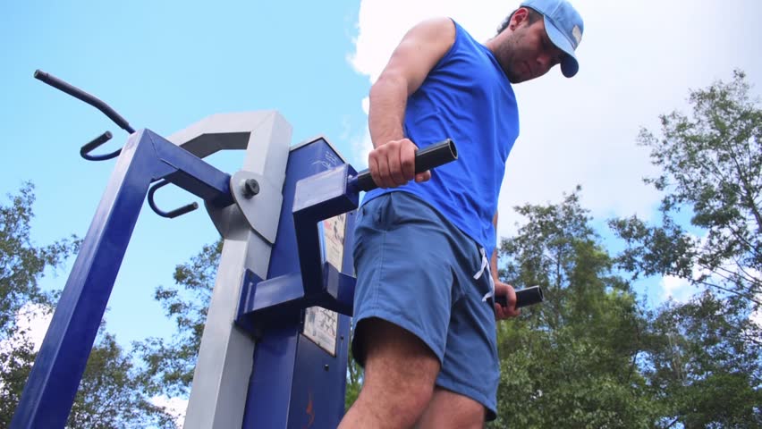 Young man doing  parallel bars excercise on gym machine in park outdoors