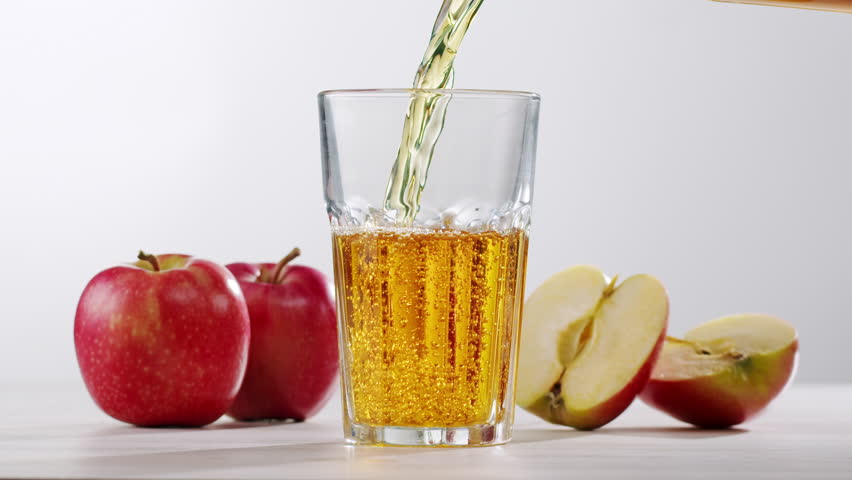 Apple juice or cider is pouring from a bottle into a glass. Fresh drink with apples and pear on an old kitchen table. 
