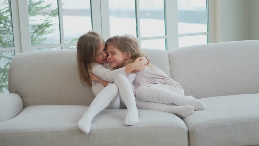 Happy family sisterly love. Two funny little twin sisters girls hugging with love care playing together at home indoors. Happy children lifestyle. Identical twin girls hugs. Girls friendship and youth