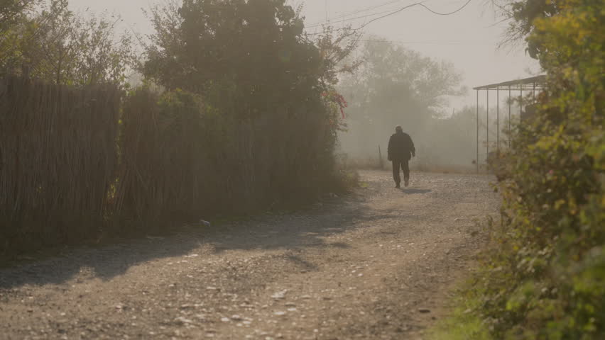 A man is walking away in a village sunset