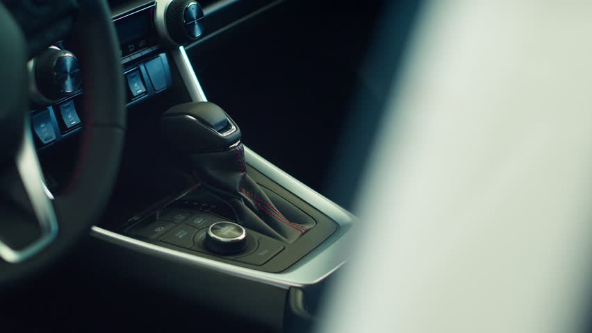Close up shot of car interior console gear lever, wheel, beverage holder and transmission control panel. Panning shot of vehicle gear shift electronic panel control buttons