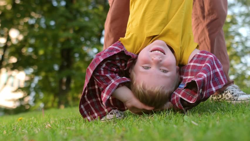 Mom and her little son are having fun together in a city park on a warm summer evening. Active family. Mom swings happy laughing boy upside down. Quality time and activity for mom and her child