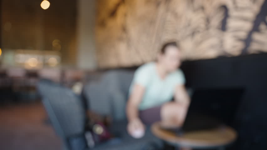 A blurred image of a woman working on a laptop in a cozy café environment, creating a relaxed and casual atmosphere ideal for productivity and focus.