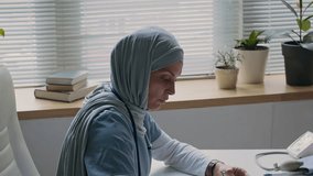 Female doctor in hijab interviewing her Muslim patients and taking notes on paper while mother holds hands with her daughter for support in medical office - Powered by Shutterstock - Get 15% off with code: PIKWIZARD15