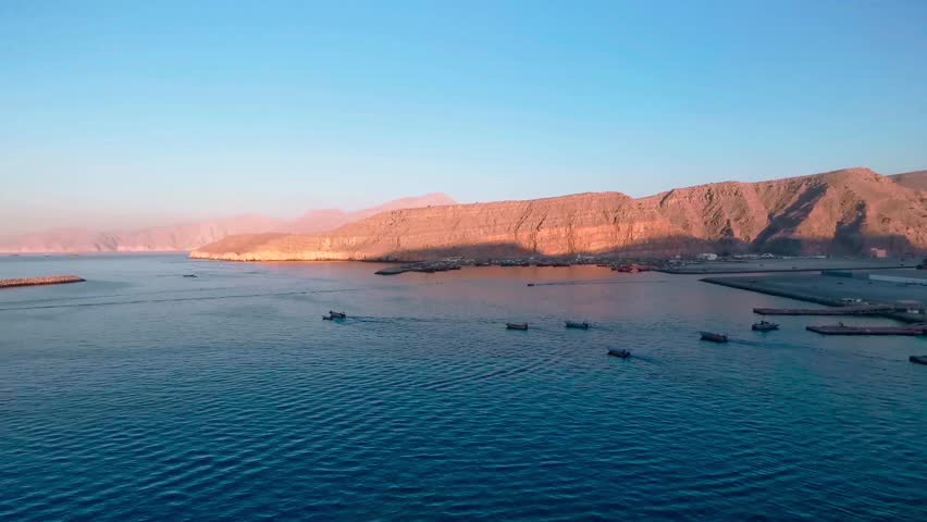 Aerial view of Oman's stunning coastline, with turquoise waters meeting golden sandy beaches. The rugged mountains in the background create a breathtaking, picturesque landscape.