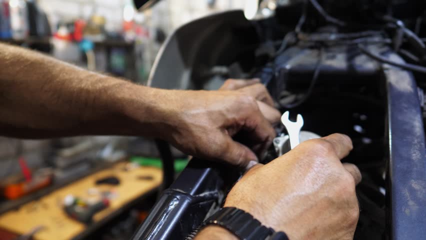 Male hands of repairer fixing moto engine at workshop. Arms of professional mechanic repairing detail of motorcycle at workplace. Adult repairman mending vehicle motor at garage. Maintenance service