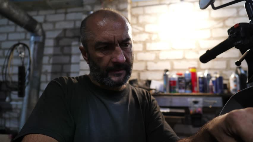 Close up of male repairer fixing moto engine at workplace. Adult mechanic repairing motor of motorcycle at workshop. Professional repairer working at garage. Concept of maintenance service. Slow mo