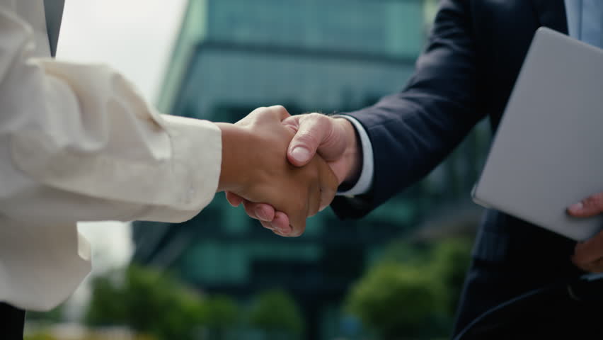 Two multiracial colleagues coworkers business partners Caucasian man businessman guy male African American woman businesswoman female girl in city handshaking shake hands partnership cooperation deal