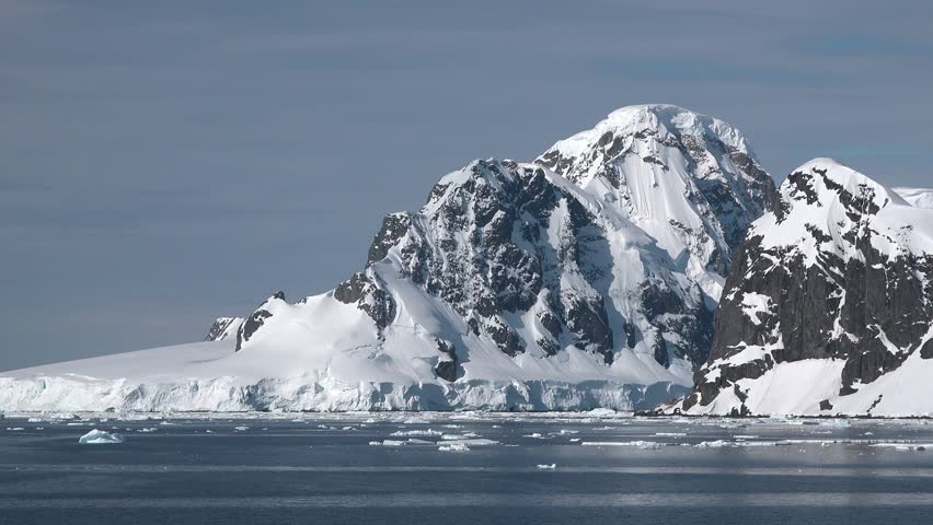 Witness the breathtaking beauty of Antarctica as large icebergs drift through calm waters near towering snowy peaks, showcasing nature