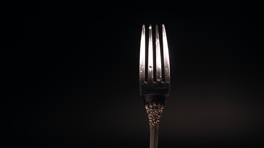 Balancing a fork on the tines in a dimly lit studio during the evening hours.