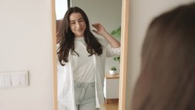 Joyful young brunette woman in casual clothes dancing and smiling while looking at her reflection in a home mirror. - Powered by Shutterstock - Get 15% off with code: PIKWIZARD15