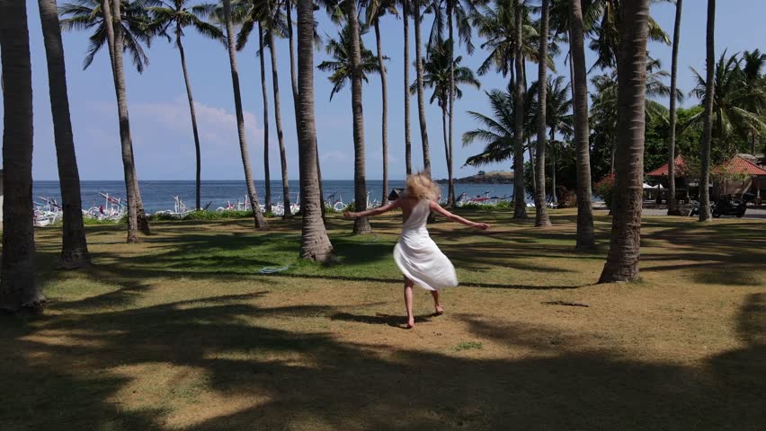 Blonde Woman Walking Through Palm Trees Near Tropical Beach.