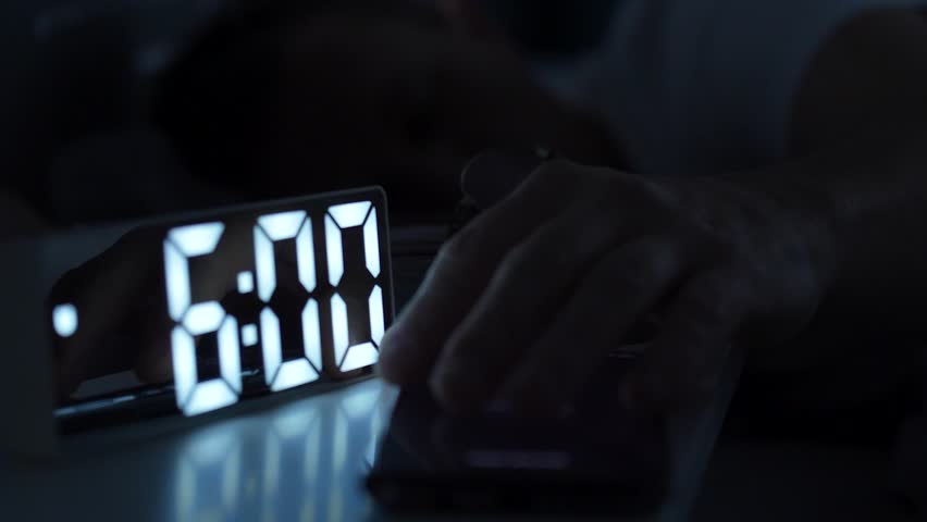 Man waking up, turning off alarm clock on digital clock and smartphone. Sleepy man waking up at 6 o'clock morning - Powered by Shutterstock - Get 15% off with code: PIKWIZARD15