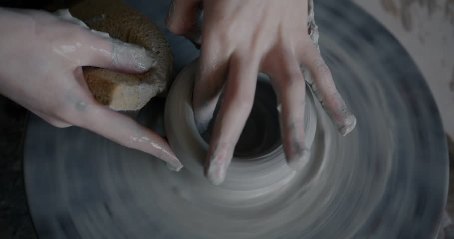 Close-up of child's hands creating pot working with clay on turning wheel in workshop while boy learning pottery. Childhood and crafts concept.