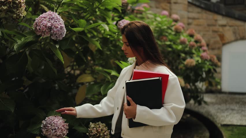 Pretty girl, student, stands with notebooks in her hands in the university garden, square, academic year, study, hydrangea, flowers, botany, confidence, adult life, university, lessons, start, tender