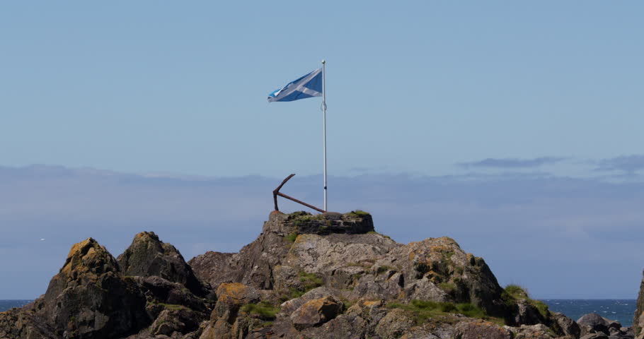 wide shot of the Scottish saltire flag on a rocky outcrop at portPatrick harbour