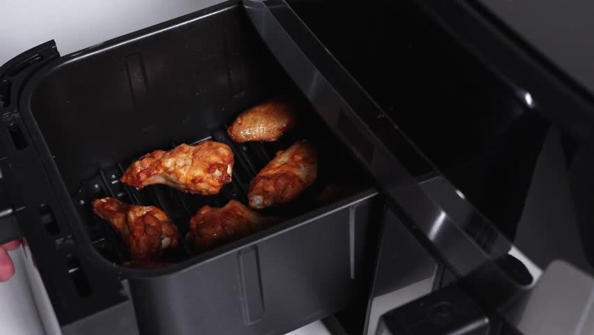 Closing air fryer with chicken wings inside, preparing for roasting