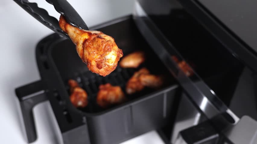 Close-up of a chicken wing freshly taken from air fryer with tongs 