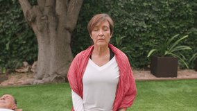 Elderly woman with eyes closed on meditation stool in peaceful home garden setting. Senior couple practicing yoga together in the morning routine. Front tracking shot, close-up, horizontal - Powered by Shutterstock - Get 15% off with code: PIKWIZARD15