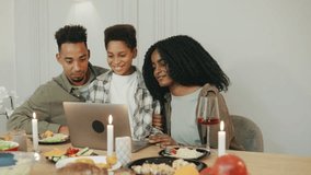 Around a holiday dinner table, an African American family connects with close friends and family through a video call, sharing joy and celebration remotely. - Powered by Shutterstock - Get 15% off with code: PIKWIZARD15