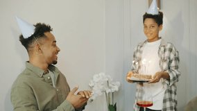 A small boy surprises his father with a festive birthday cake topped with candles. The African American family celebrates joyfully around the table, sharing smiles and love. - Powered by Shutterstock - Get 15% off with code: PIKWIZARD15