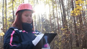 European female volunteer in a helmet with a tablet checking trees. Female environmental technician looking at tree tops. Forestry engineer. Control supervision of a nature reserve - Powered by Shutterstock - Get 15% off with code: PIKWIZARD15