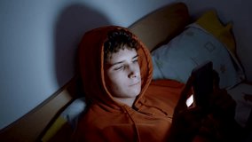 4k medium handheld shot of teenager using a smartphone lying in bed late at night, playing games, watching videos, and scrolling the screen. Children's screen addiction. Screen Addiction in Youth. - Powered by Shutterstock - Get 15% off with code: PIKWIZARD15