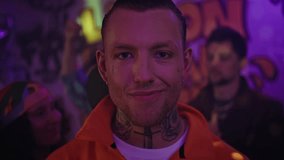 Tattooed man at party neon glow looking camera defiantly closeup. Portrait of cool male clubber standing in vibrant club atmosphere. Handsome guy model posing on dance floor enjoying vivid discotheque - Powered by Shutterstock - Get 15% off with code: PIKWIZARD15