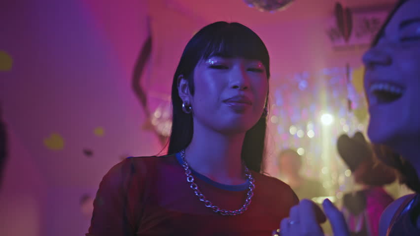 Asian woman dancing at party in vibrant nightclub closeup. Carefree brunette moving body in red dress feeling happiness in disco bar. Happy girl with glitter makeup enjoy weekend entertainment in club