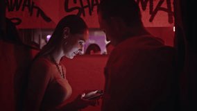 Dating woman holding mobile phone talking with boyfriend bathed in red neon light closeup. Romantic couple meeting in modern nightclub with graffiti wall. Smiling girl writing telephone number to guy - Powered by Shutterstock - Get 15% off with code: PIKWIZARD15