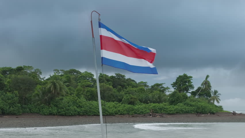 A stunning view of the Costa Rican flag waving at Nasua Coati Beach, surrounded by tropical scenery and a colorful sky, captured in sharp 4K resolution
