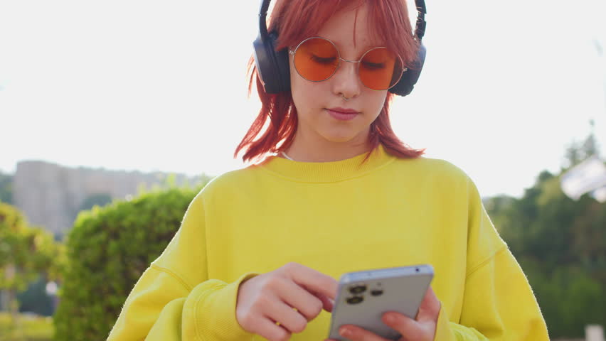teenage girl with bright hair and facial piercings who uses the phone and listens to music on headphones. Teenage girl music lover enjoying music.