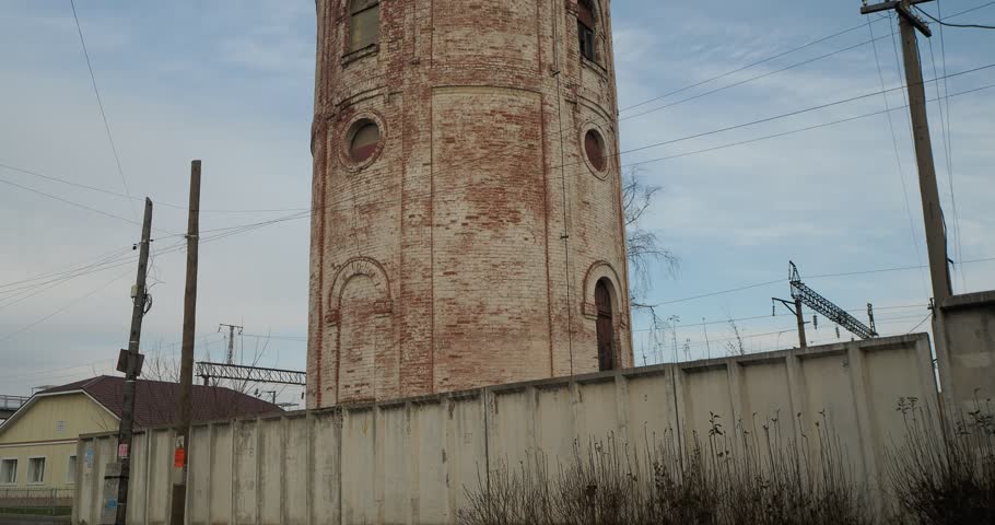 Building. An old inactive brick water tower stands on a city street behind a concrete fence. Hand held, Siberia.