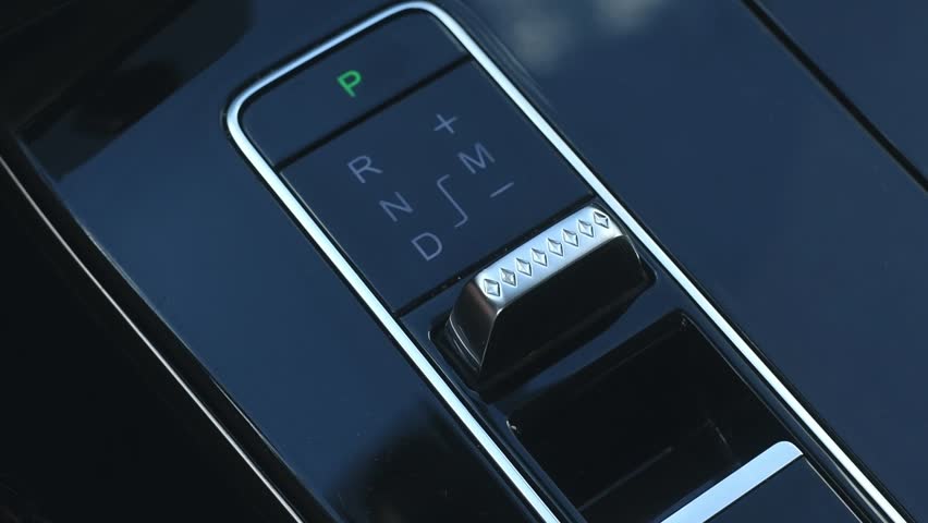 Minimalist gearshift knob of the automatic transmission of a modern automobile. Man's hand shifts speeds of automatic transmission.