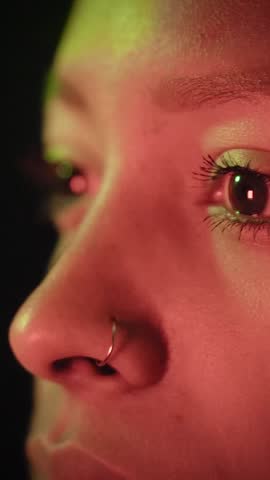 Vertical. Woman Face with Open Eyes in Colorful Neon Light of TV television news. Pretty Girl Looking Around in Modern Studio. Flickering Multi-Colour on Skin and Facial Features of Female